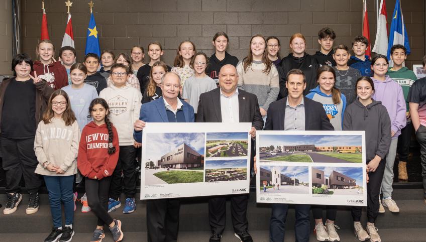 image of a group of students with three adults in front of them holding design renditions of a school