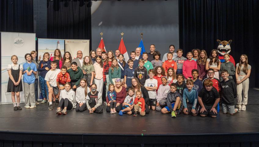 roupe de jeunes étudiants et de quelques adultes sur une scène de spectacle avec des drapeaux en arrière-plan