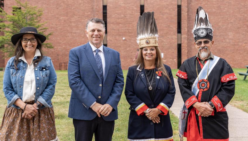 image of four people standing shoulder to shoulder with a brick building in the background