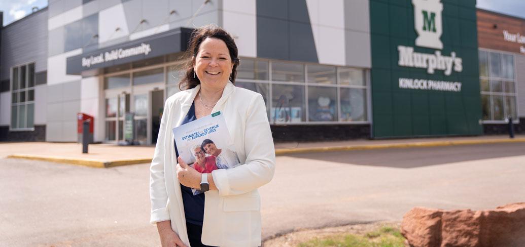 image of a person standing in front of a pharmacy while holding budget document