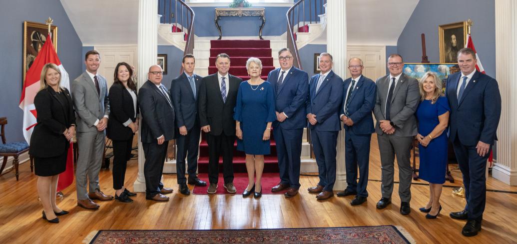 image of a group of people standing shoulder to shoulder inside a stately room in front of stairs