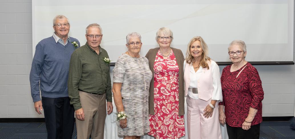 image of six people standing shoulder to shoulder in front of a projector screen