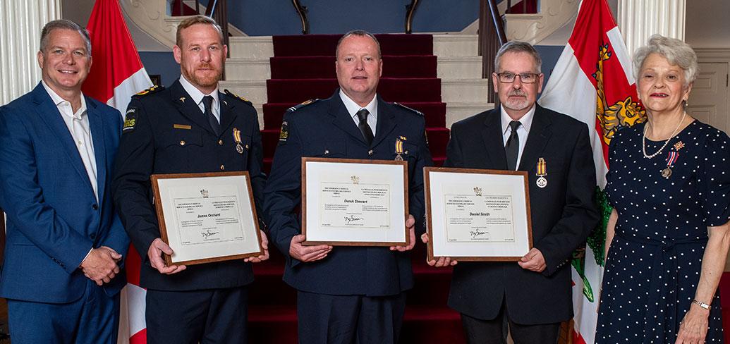 image of five people standing shoulder to shoulder with the middle three holding framed certificates
