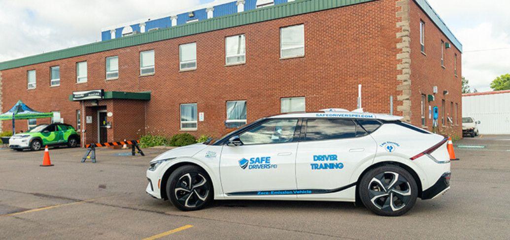 image of an electric vehicle in the parking lot of a brick building in the background