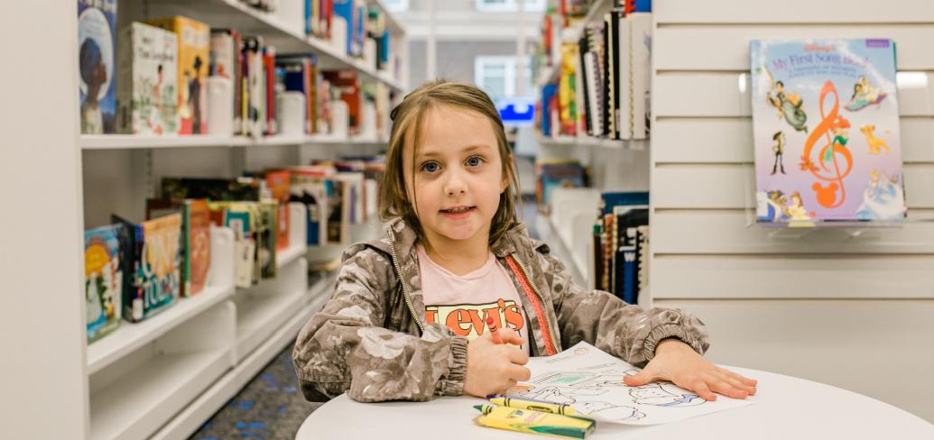 image of a child sitting at a table colouring with crayons in a libraray