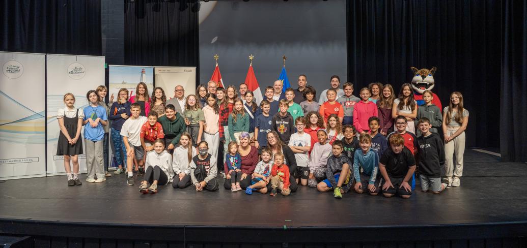 image of a large group of young students and some adults on a performance stage with flags in the background