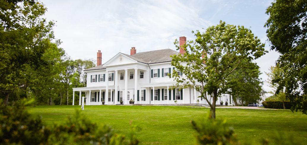 image of a large stately home with a large grass area and various trees surrounding it.