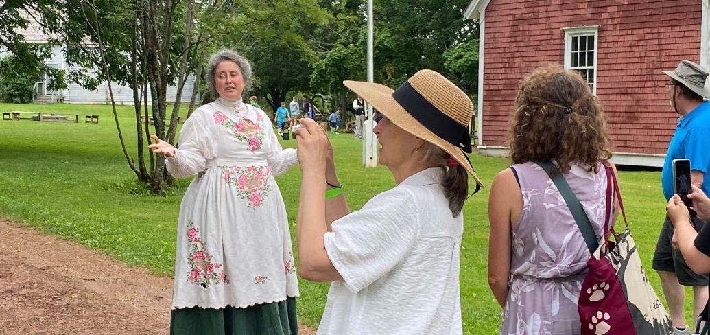 image of a person in 1800s clothing speaking to some people outside a barn