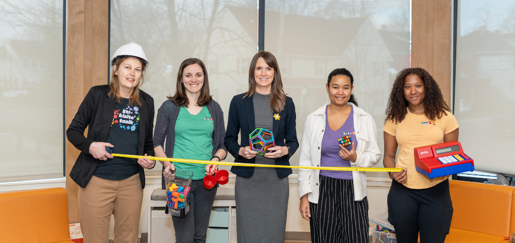 image of  five people standing shoulder to shoulder inside a building while holding some play objects