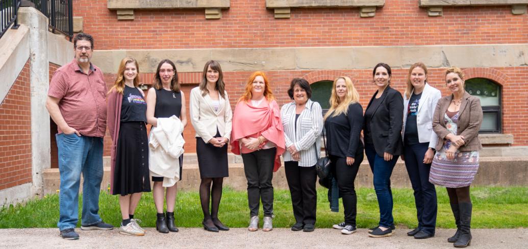 image of a group of people standing shoulder to shoulder in front of a red brick building