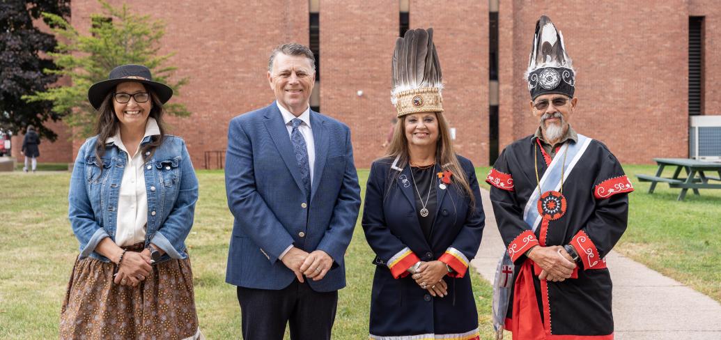 image of four people standing shoulder to shoulder with a brick building in the background