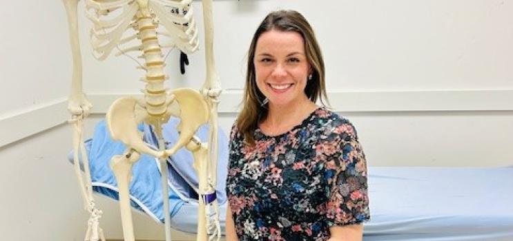 A woman, a physiotherapist, poses in front of a skeleton 