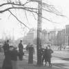 People stroll along a busy street in a historic city scene.