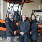 image of three people in front of a small rescue boat inside a garage