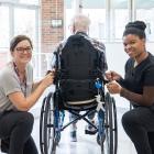 image de deux personnes à côté d'une personne en chaise roulante à l'intérieur du hall d'un immeuble