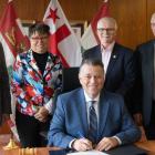 image of four people standing behind and overlooking a person while someone sits at the desk signing a proclamation