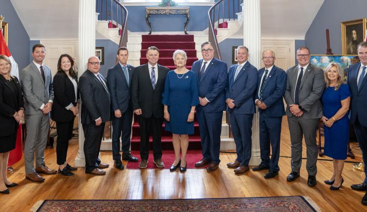 image of a group of people standing shoulder to shoulder inside a stately room in front of stairs